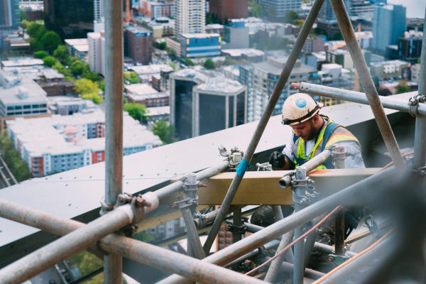 A construction worker working on a roof structure high above a city seen in the background.